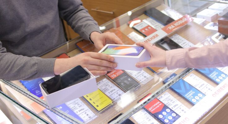 Penjual dan pembeli bertukar ponsel di toko handphone, ilustrasi KBLI konter pulsa dan toko HP