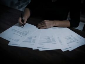 Wanita memeriksa tumpukan dokumen di meja, ilustrasi legalitas dan KBLI usaha