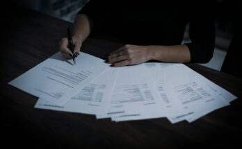Wanita memeriksa tumpukan dokumen di meja, ilustrasi legalitas dan KBLI usaha