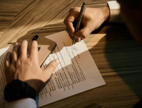 Tangan menandatangani dokumen di atas kertas, ilustrasi perbedaan pendirian PT online dan lewat notaris