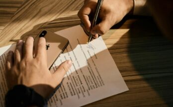 Tangan menandatangani dokumen di atas kertas, ilustrasi perbedaan pendirian PT online dan lewat notaris