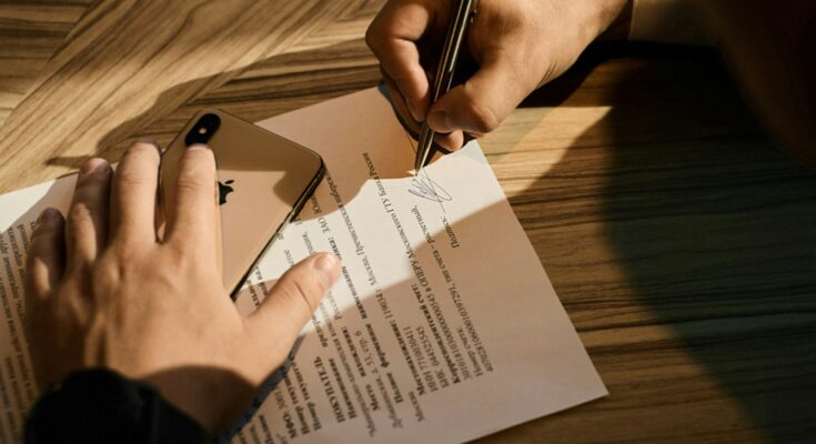 Tangan menandatangani dokumen di atas kertas, ilustrasi perbedaan pendirian PT online dan lewat notaris